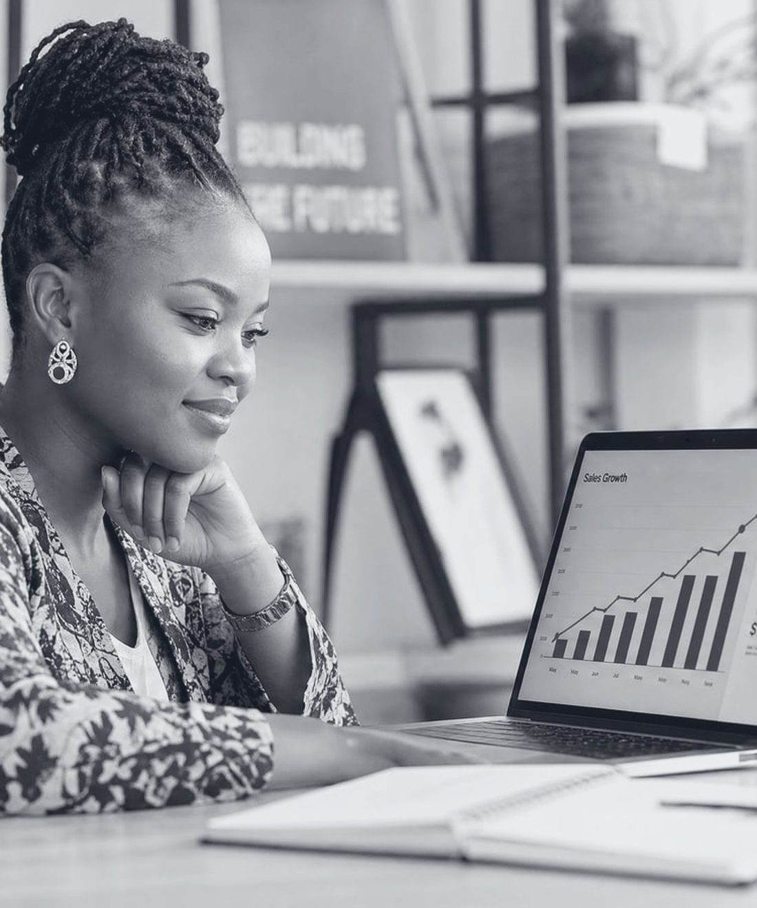 An African founder at her desk reviewing a rising sales growth chart on her laptop.